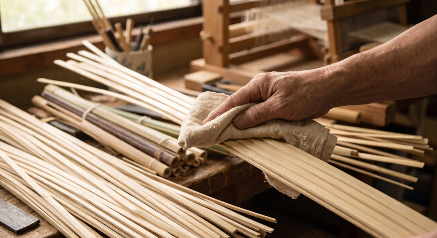 A craftsman wiping split bamboo strips with a soft cloth on a workshop bench